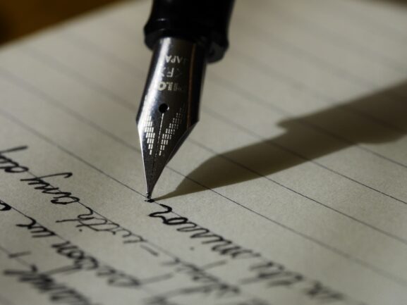 Person writing with a pen, representing writing an effective classified ad