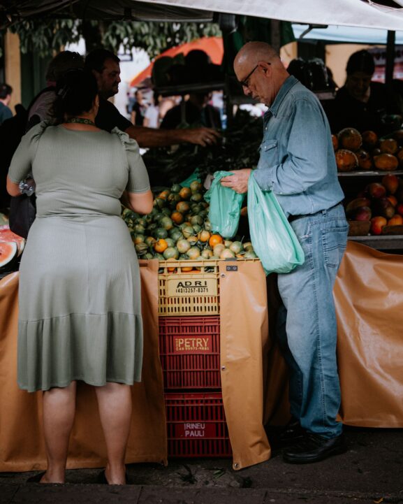 A busy outdoor local market scene with shoppers browsing stalls, representing community-driven commerce