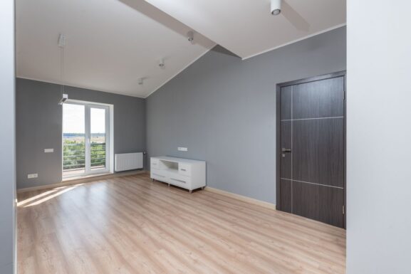 Bright, empty modern apartment room with hardwood floors and large window, representing a first NYC apartment rental