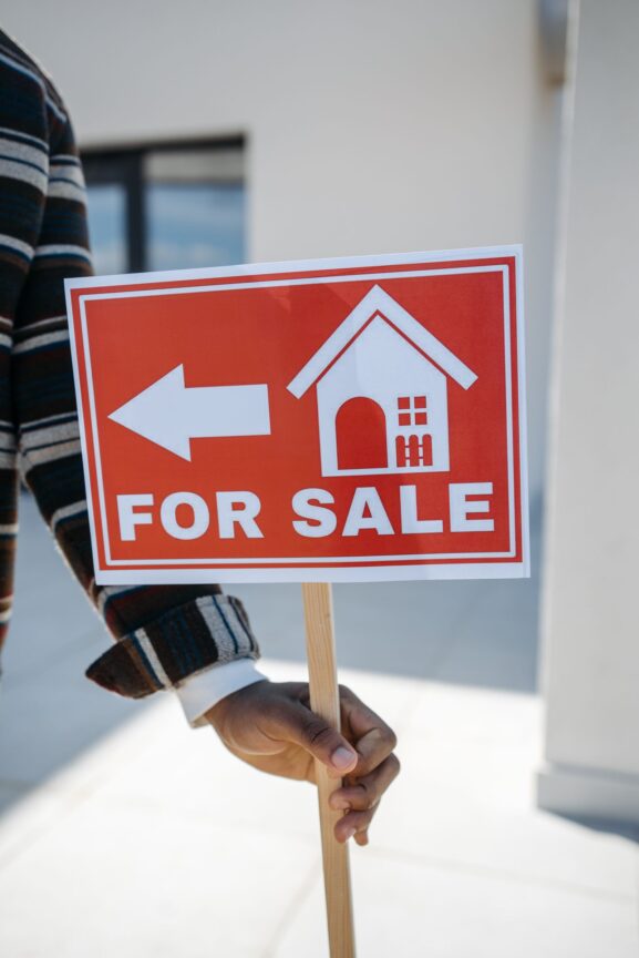A "for sale" direction sign held up outside a home, symbolizing a homeowner ready to list their property
