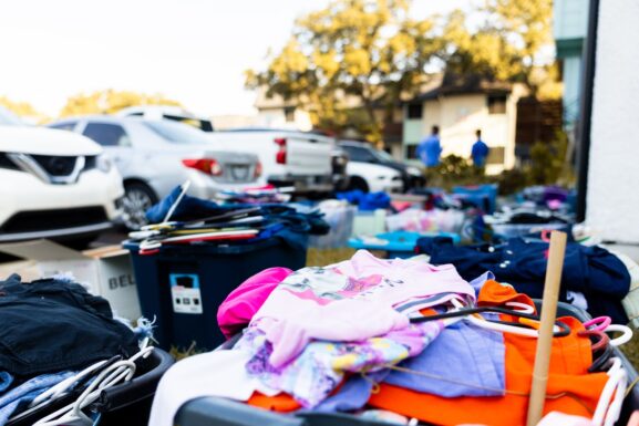 An outdoor garage sale with clothes and items displayed for sale in a driveway