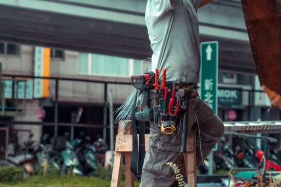 A local handyman wearing a tool belt while standing on a ladder during a repair job