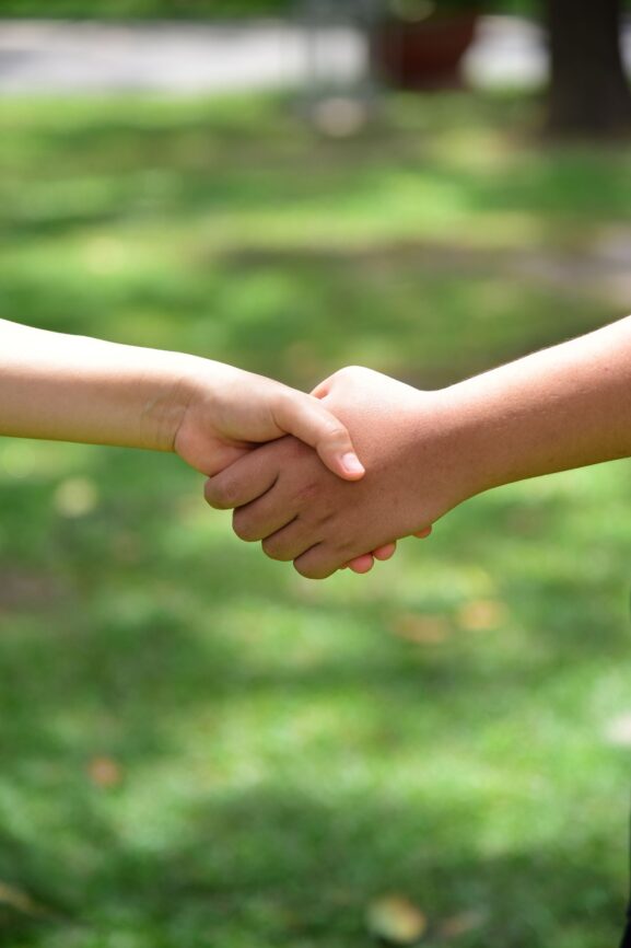 Two people shaking hands outdoors in a sunlit public park, representing a safe in-person meetup between a buyer and seller
