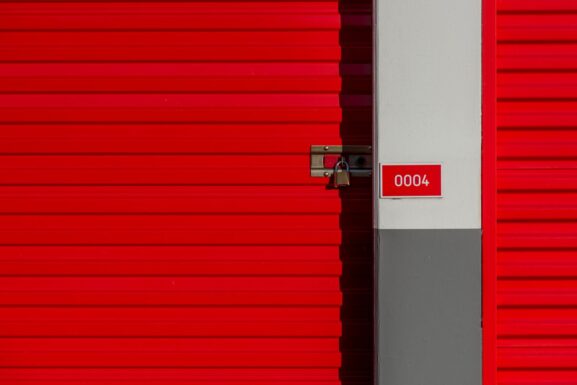 A red storage unit door secured with a padlock and marked with a unit number