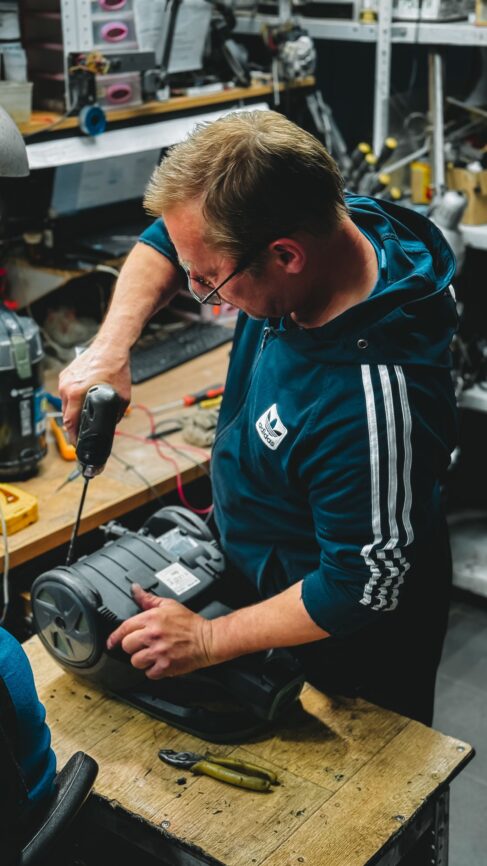 A man using a power drill in a workshop while repairing equipment