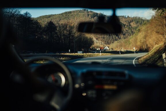 View of an open road leading toward distant mountains, seen through a car windshield during a weekend road trip