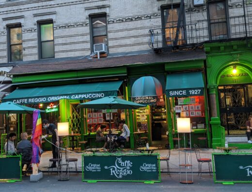 Green storefront of Caffe Reggio on MacDougal Street in Greenwich Village, New York, with outdoor tables and its Original Cappuccino sign