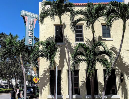 Joe's Stone Crab restaurant building with its vertical neon sign and palm trees on Washington Ave in Miami Beach