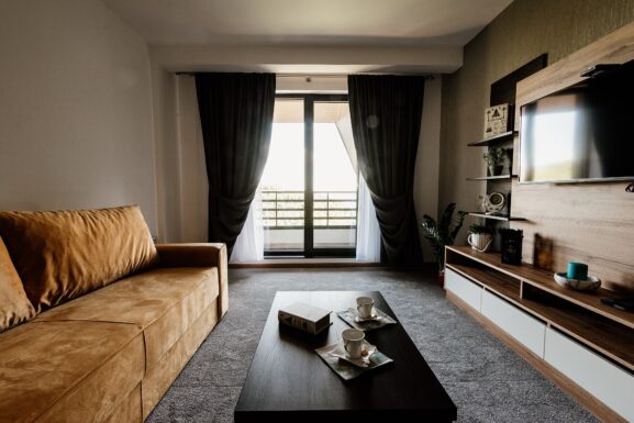 Bright modern apartment living room with a tan sofa, coffee table, TV wall and balcony doors