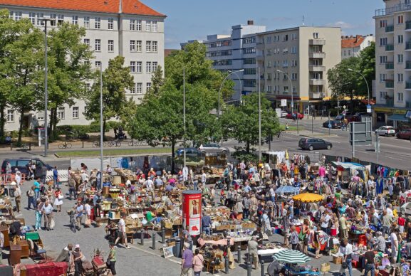 Crowds browsing rows of stalls at a large outdoor neighborhood flea market on a sunny day
