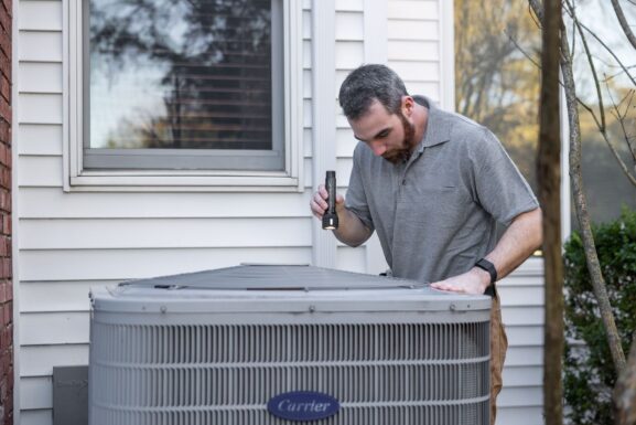 Local HVAC technician inspecting a home heat pump unit before winter