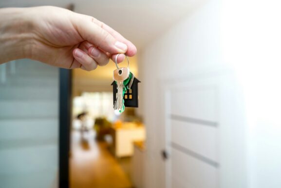 A hand holding a set of house keys in front of a home entrance